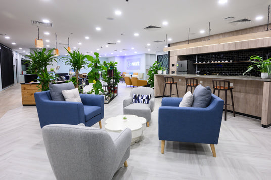A casual meeting area outside our pantry is pictured here. A small flower-shaped table sits in the centre of four facing armchairs. All the armchairs boast comfortable cushions. Greenery can be found around the meeting area. 