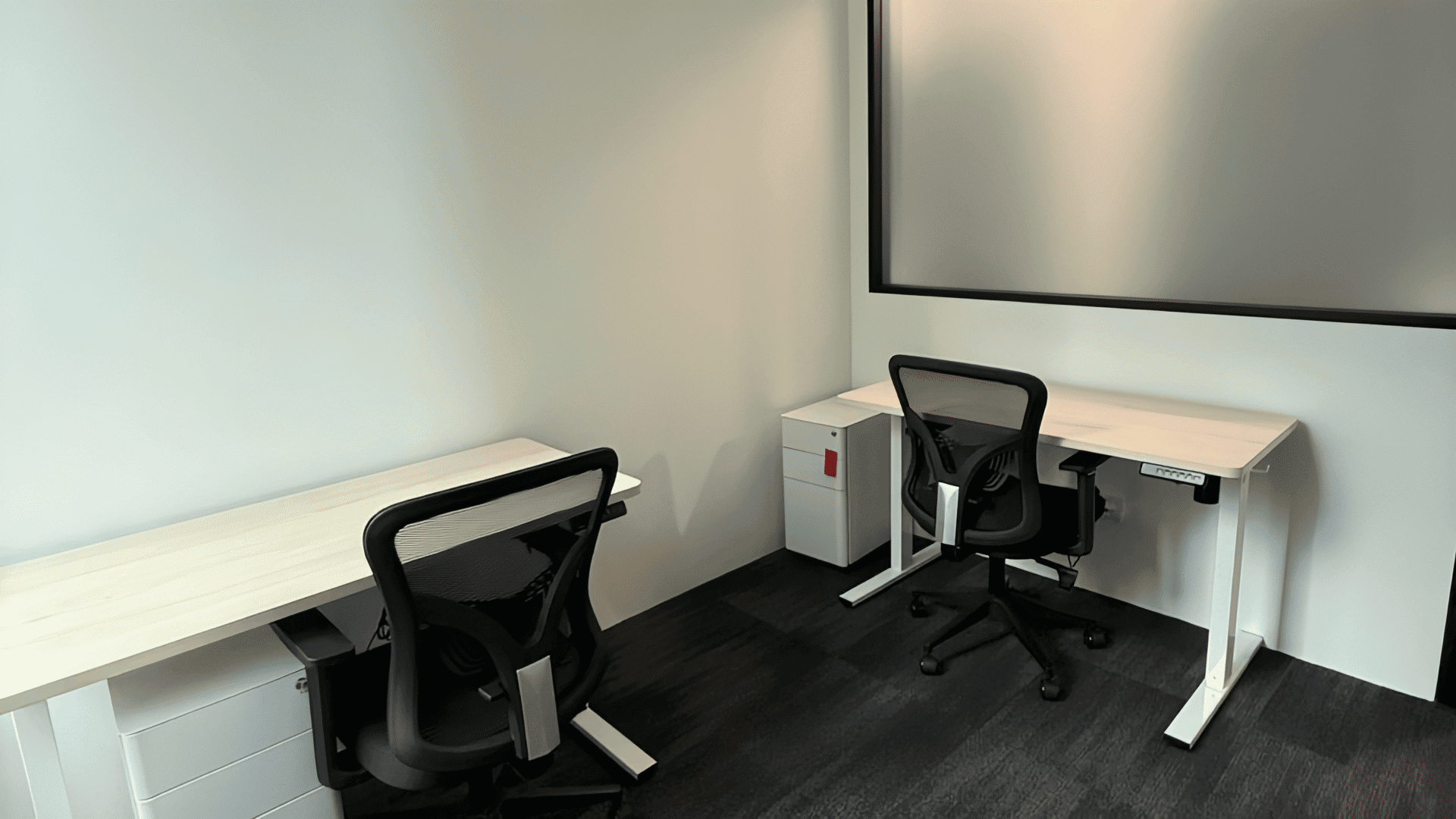 A clean, well-lit coworking area featuring two desks and comfortable chairs for flexible work.