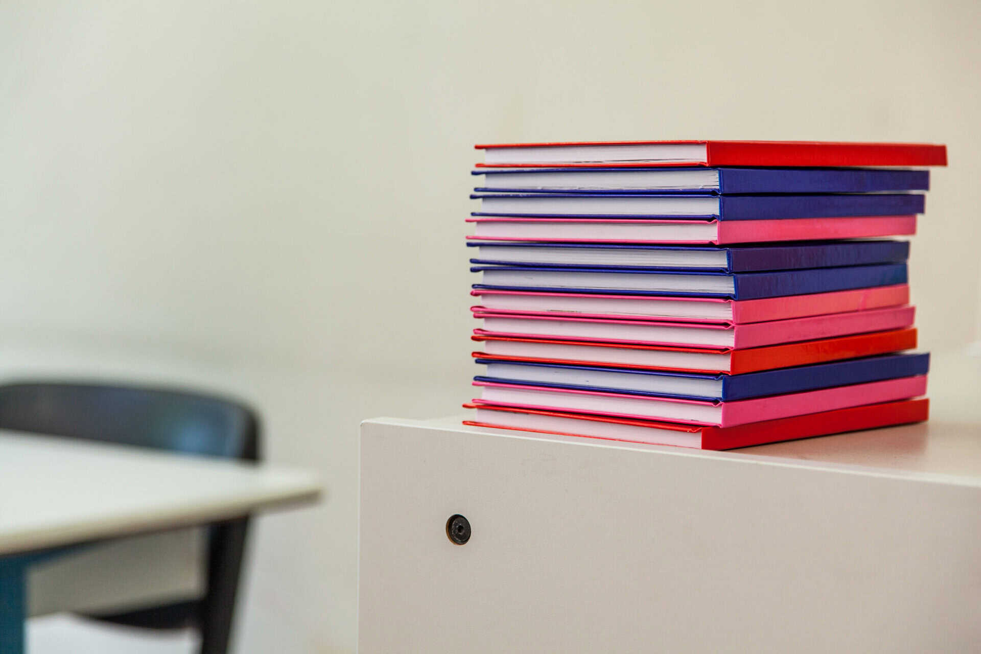 Stack of colourful notebooks on a white desk in a coworking space.