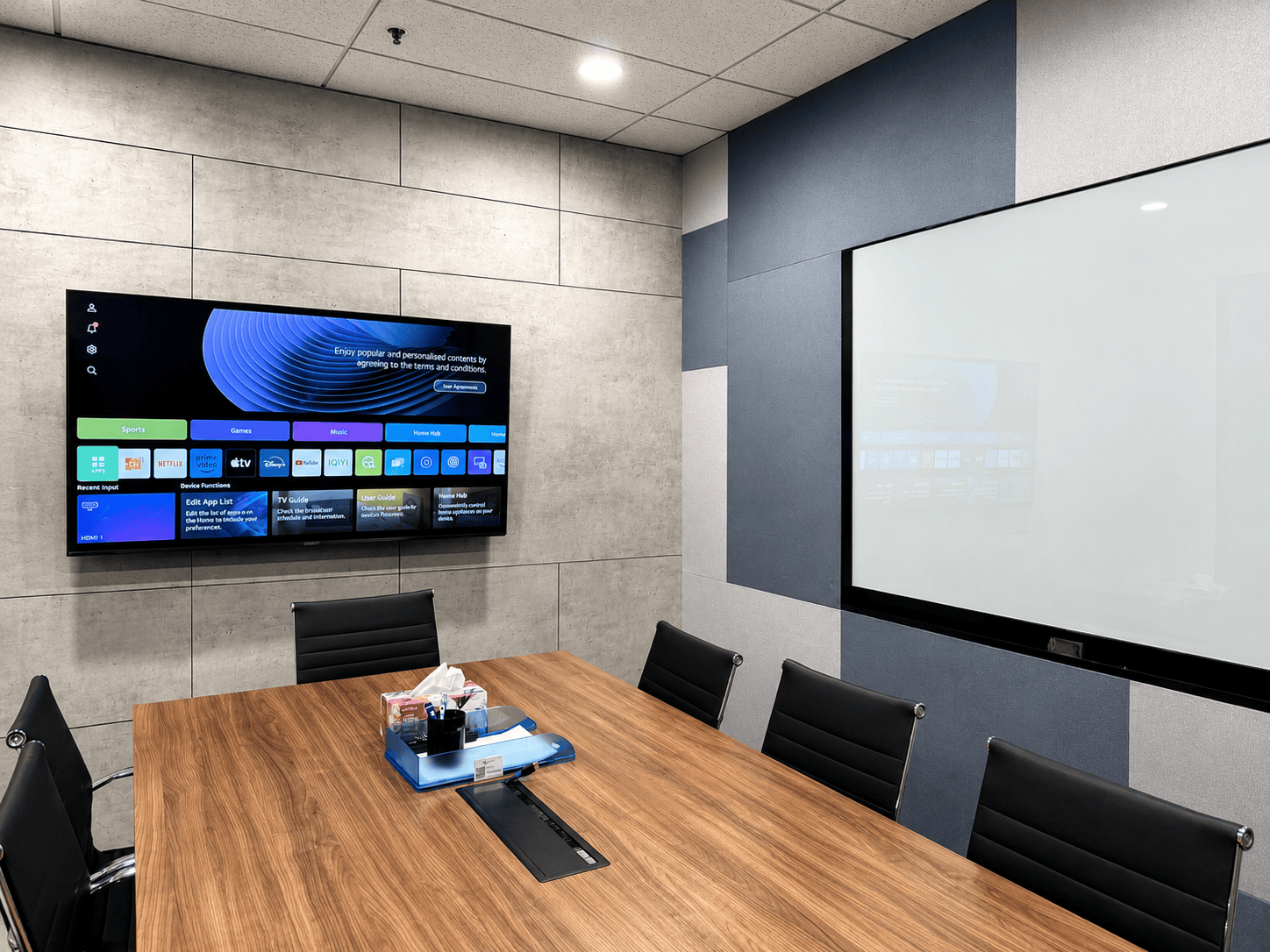 Modern coworking meeting room with large screen and wooden table.