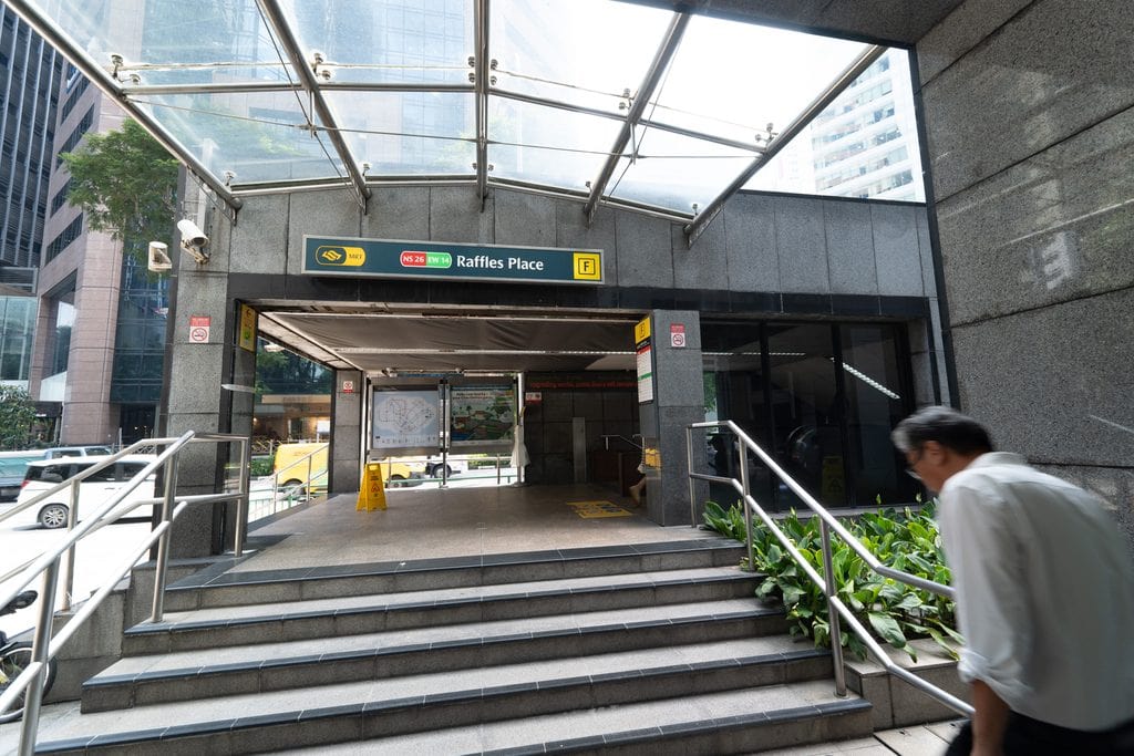Entrance to Raffles Place MRT station in Singapore with escalators and signage.
